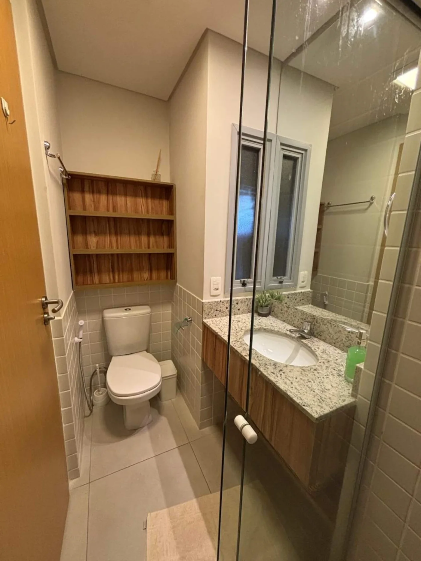 Banheiro moderno e funcional, equipado com chuveiro e box de vidro, garantindo praticidade e conforto durante o uso. Ambiente limpo e organizado, ideal para uma experiência agradável no dia