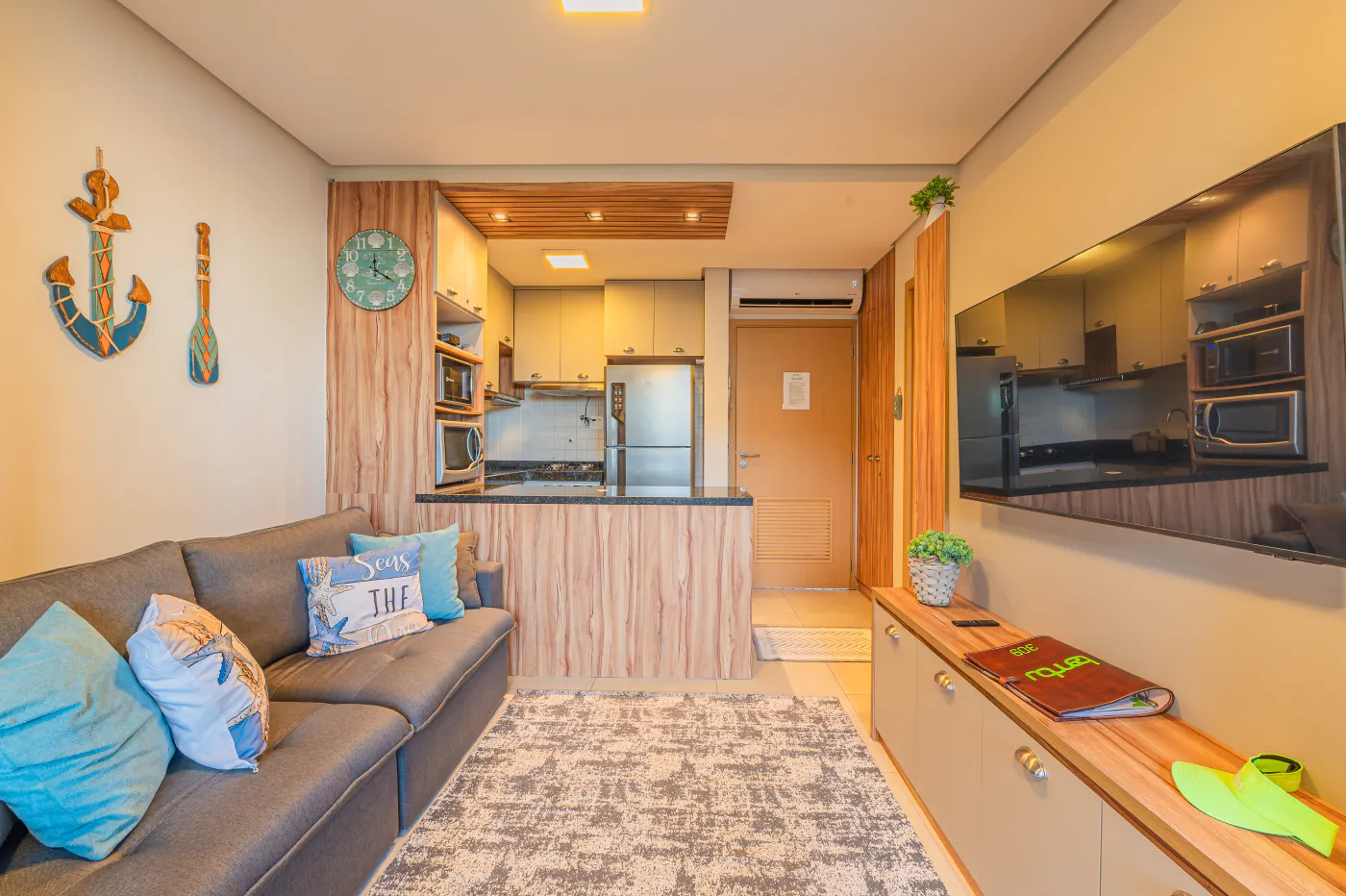 Sala integrada do apartamento: sofá, tapete, TV e a cozinha ao fundo