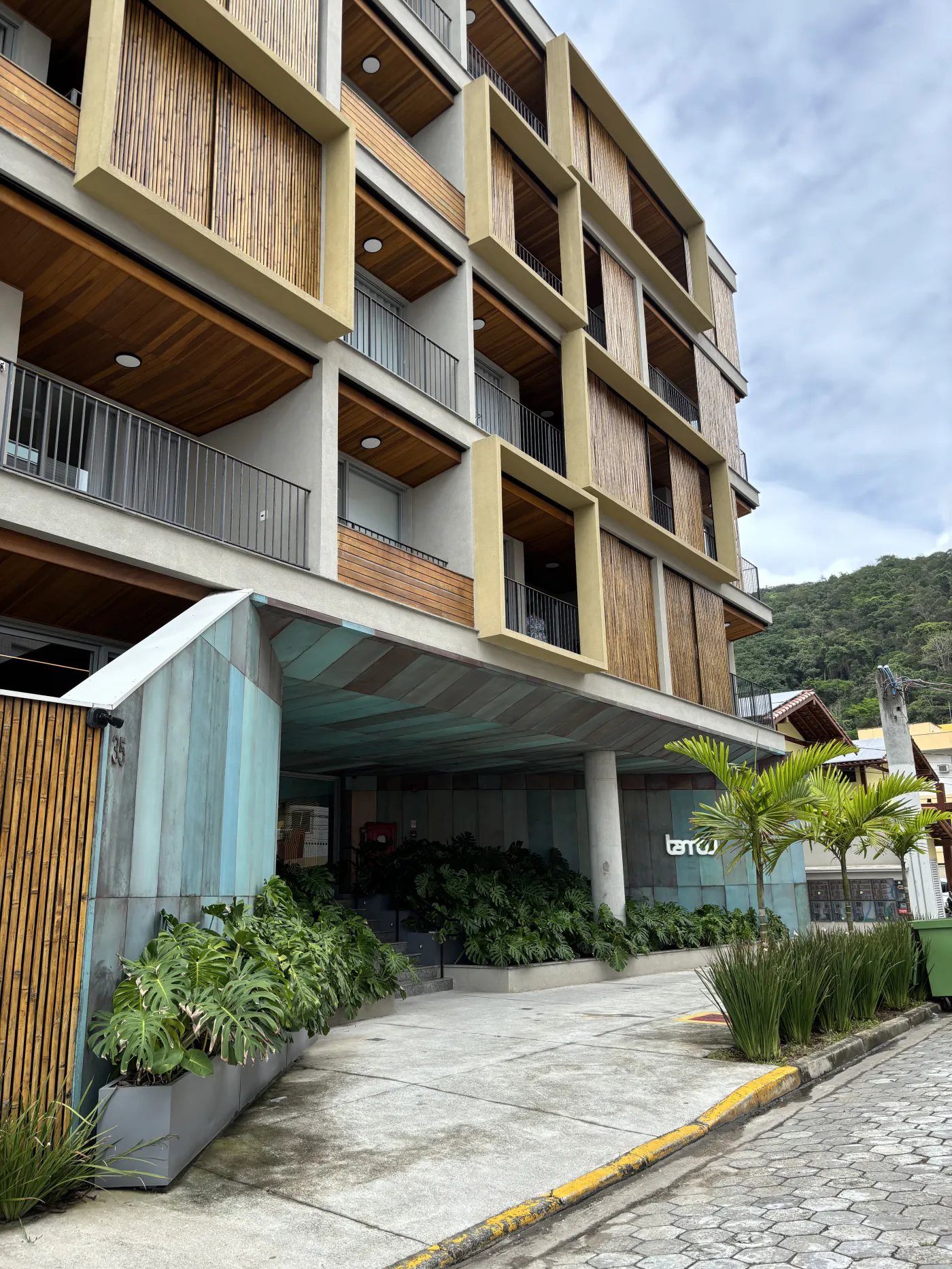Fachada do Condomínio Bambu na Praia Grande, com brises de madeira e entrada entre jardins