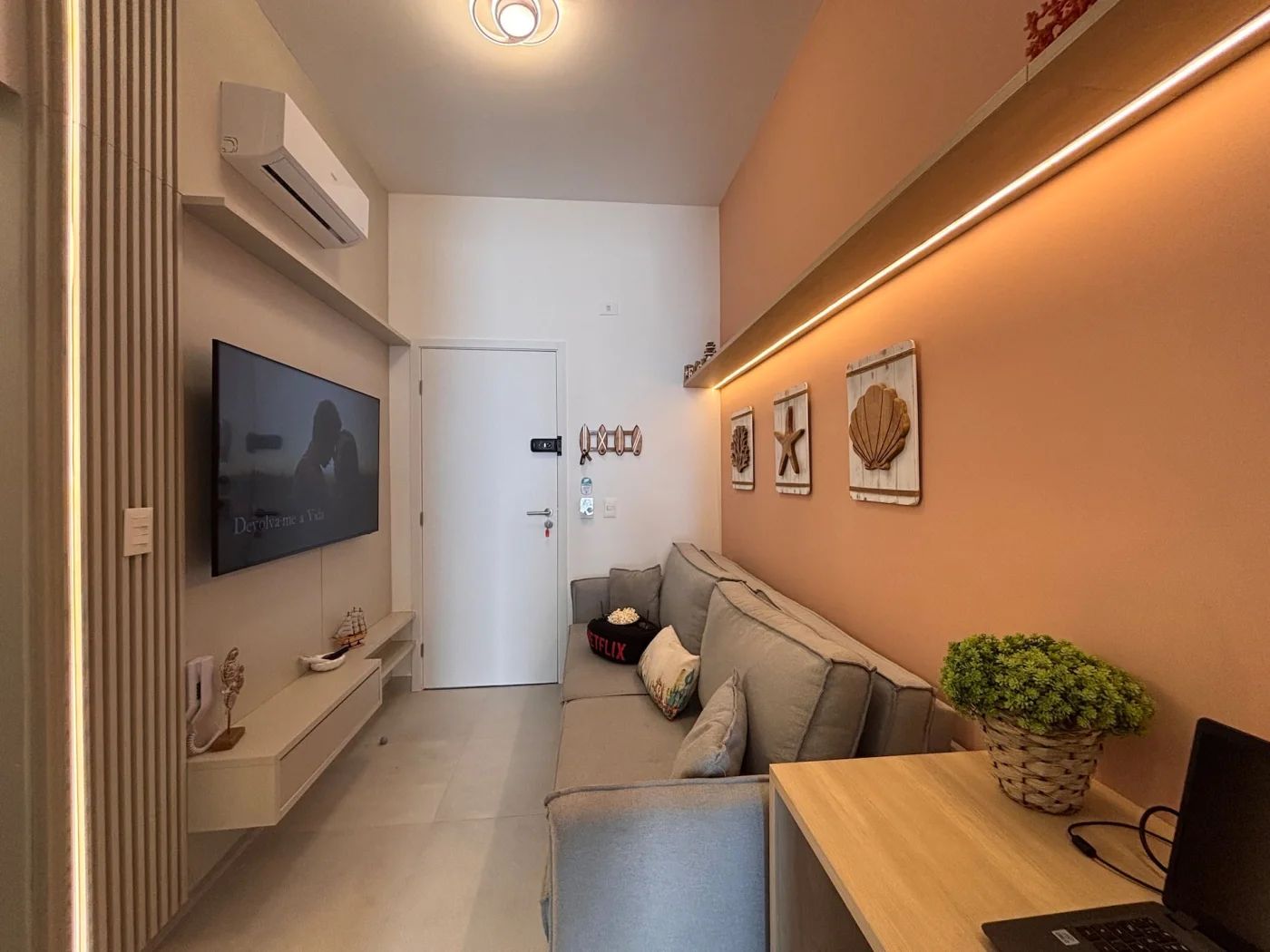 Sala de estar com decoração praiana que transmite aconchego e tranquilidade. Tons claros, coral e bege predominam, combinados com móveis planejados. Almofadas macias, mantas leves e luz suav