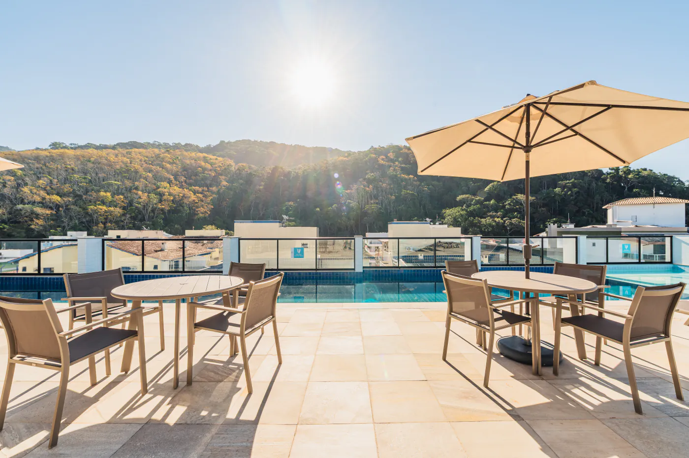 Piscina da cobertura com guarda-sol, mesas e as montanhas ao fundo